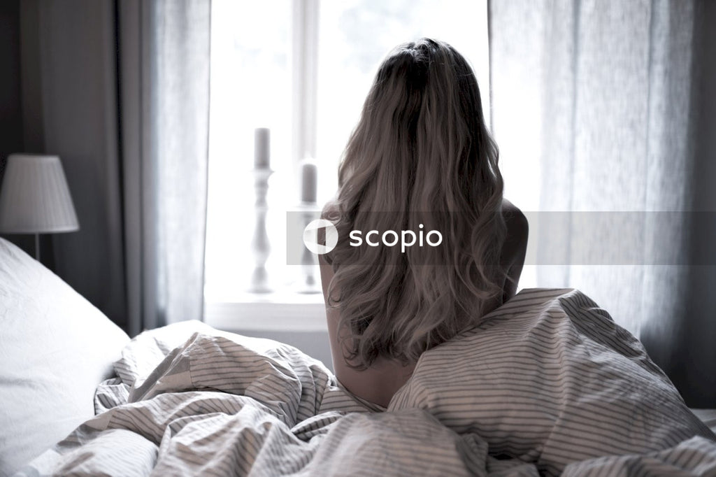 Backside of topless woman facing window while sitting on bed