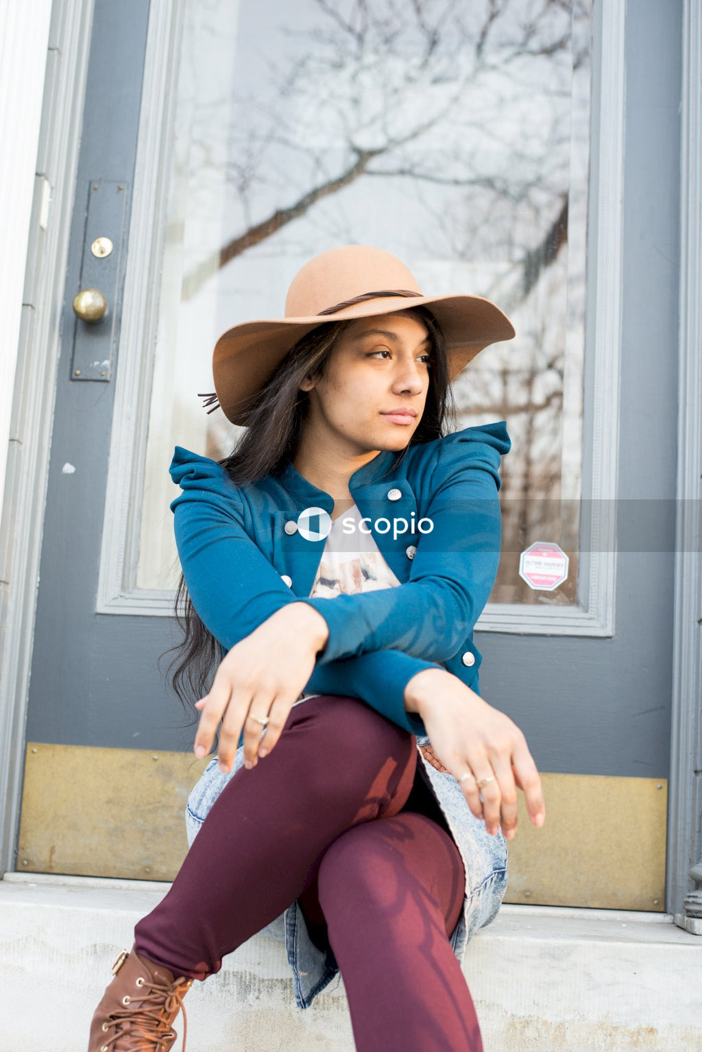Woman in blue denim jacket and brown cowboy hat sitting on front step