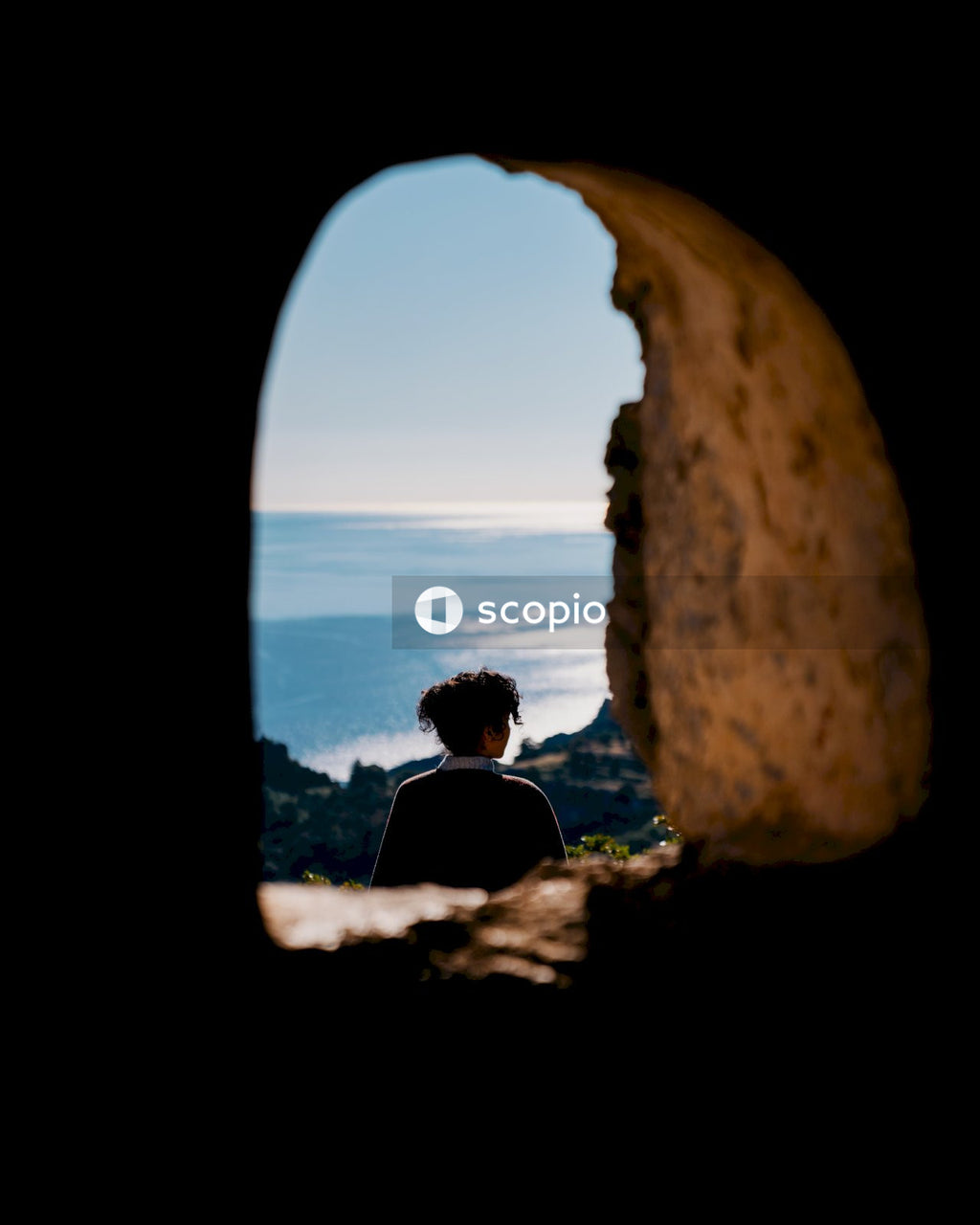 Man in black shirt sitting on rock near sea