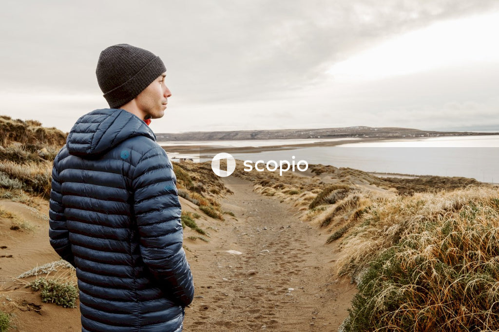 Man in black knit cap and black jacket sitting on brown sand near sea