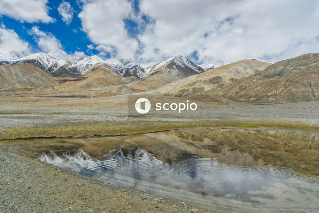 Brown and white mountains beside lake under blue sky