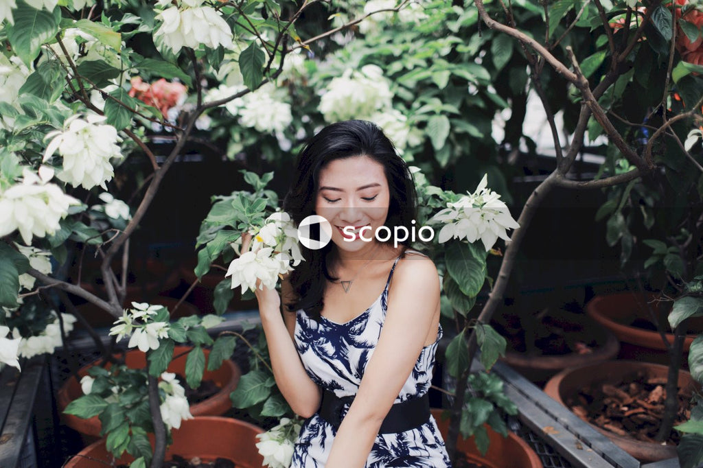 Woman in light and dark jumpsuit sitting near bush holding light flower