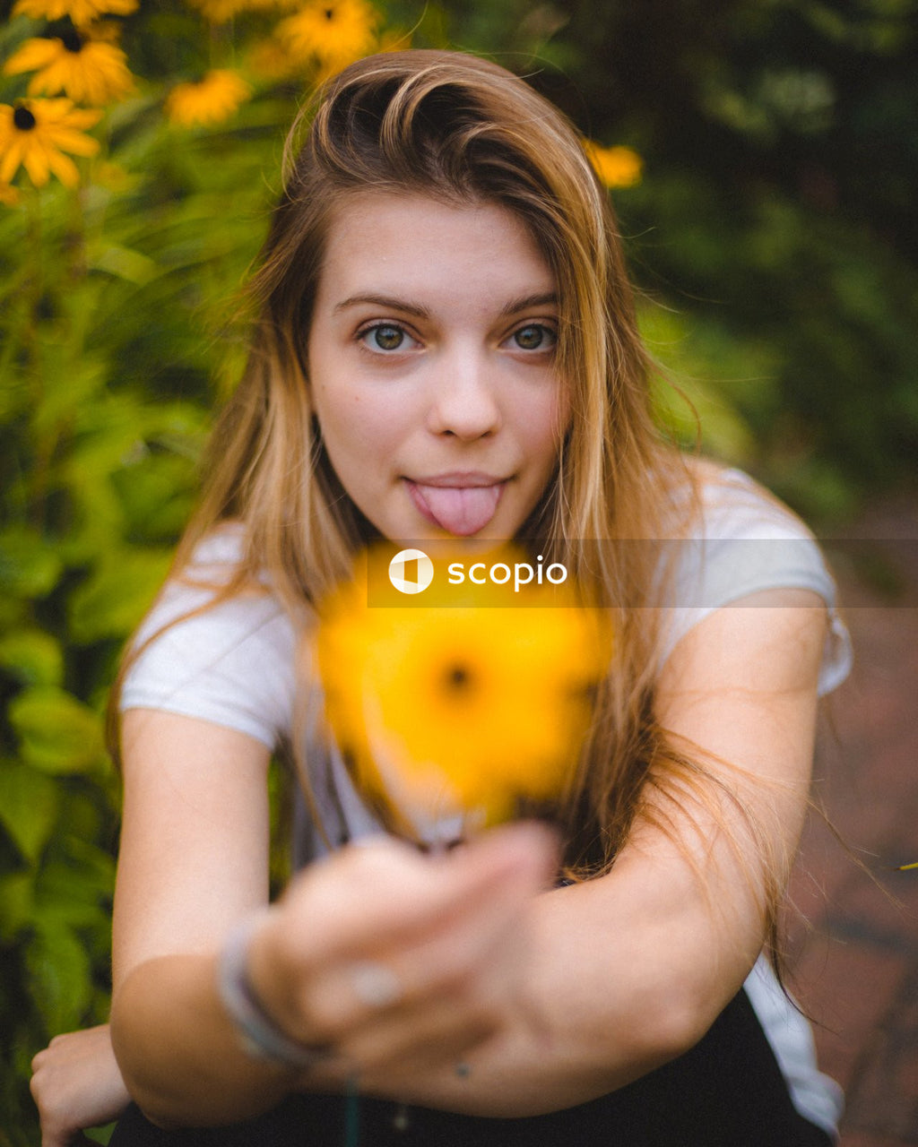 Blonde woman poking her tongue and holding yellow flower