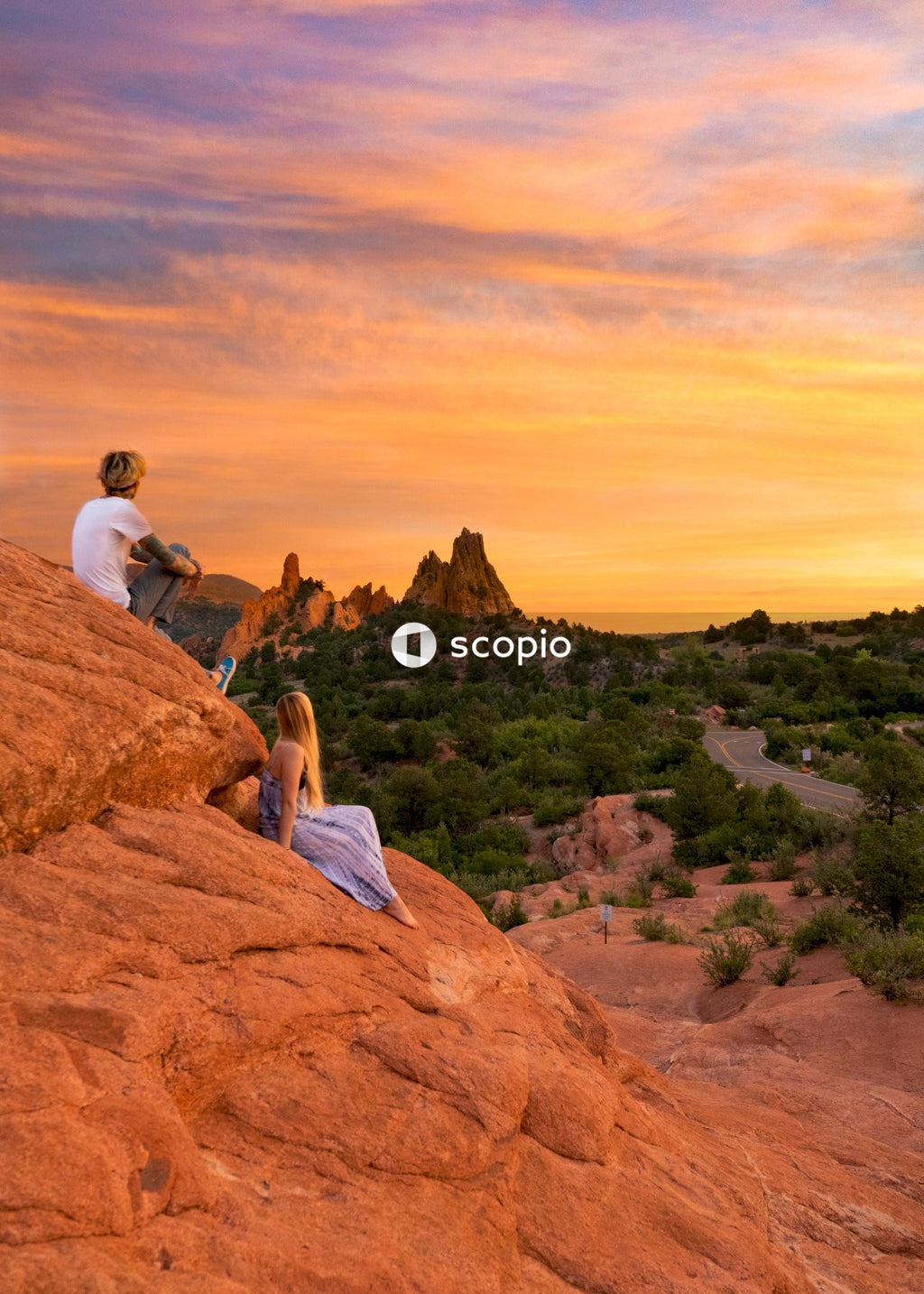 Man and woman sitting on brown rock formation watching the sunset