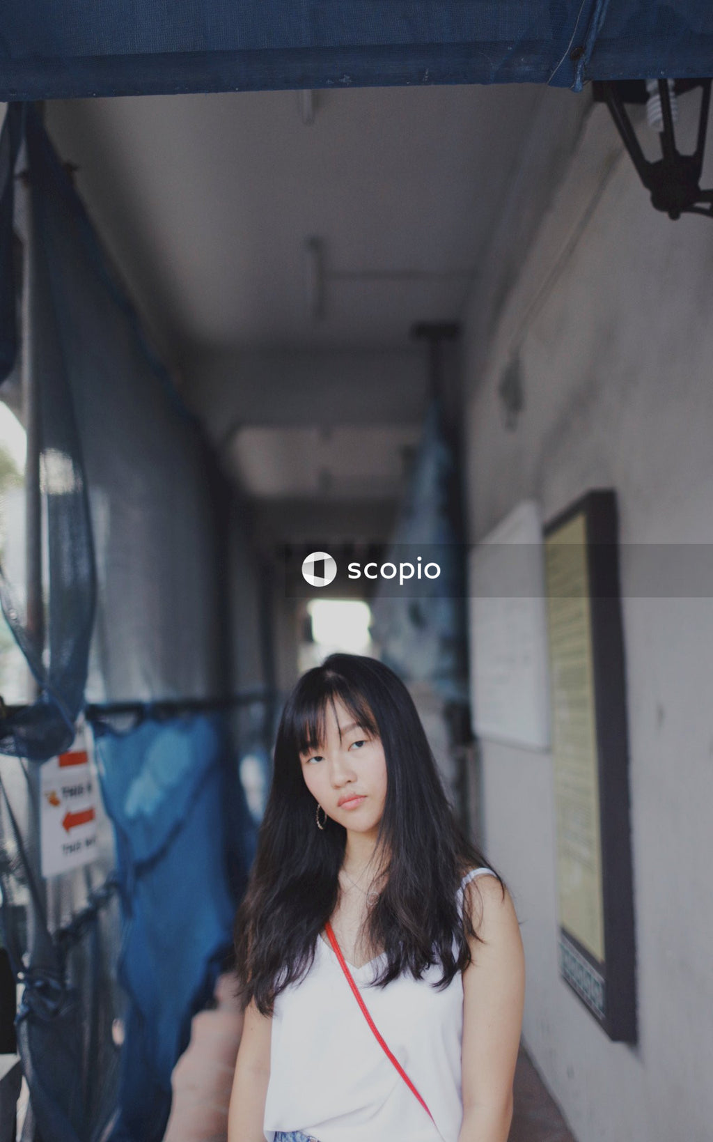 Woman wearing a white tank top with black hair stands in a hallway