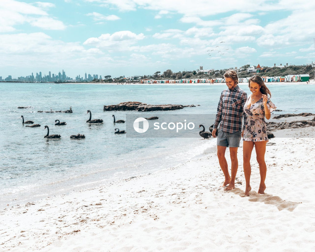 Man and woman walking on seashore near ducks floating on the sea