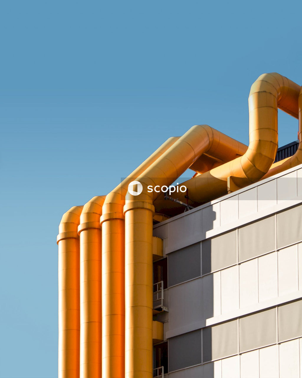 Four yellow pipes on white wall outdoor under blue sky