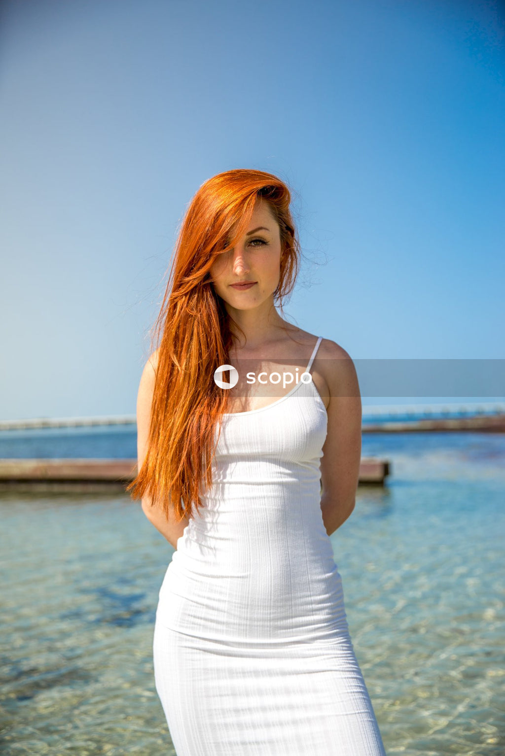 Woman in white spaghetti strap top standing near body of water