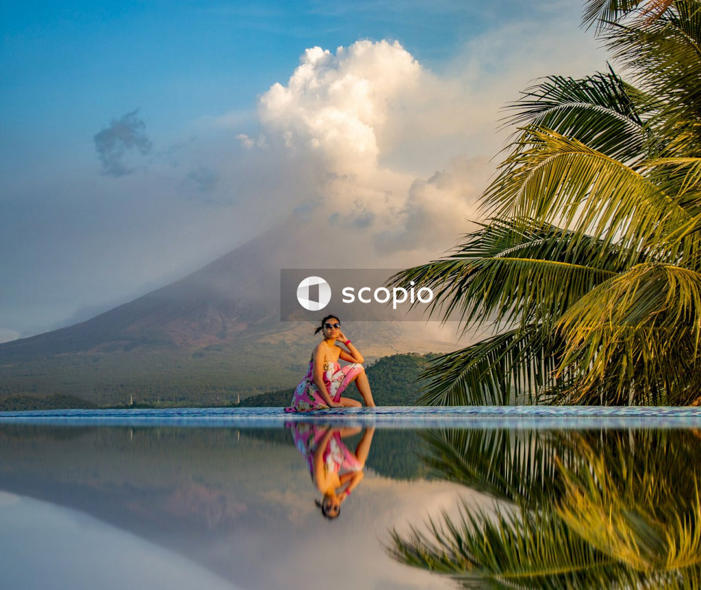 Woman in orange and blue jacket sitting on green palm tree near body of water