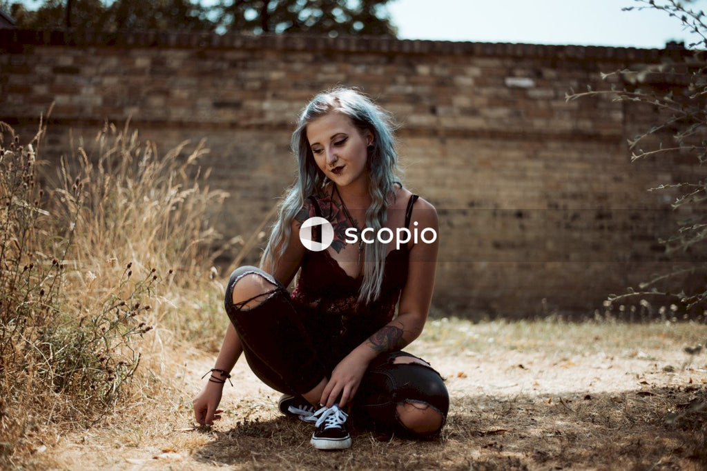 Young blonde tattooed woman with dyed blue hair sitting on brown field