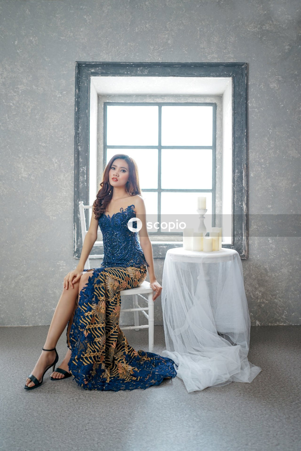 Woman in blue long dress sitting on light wooden chair indoor