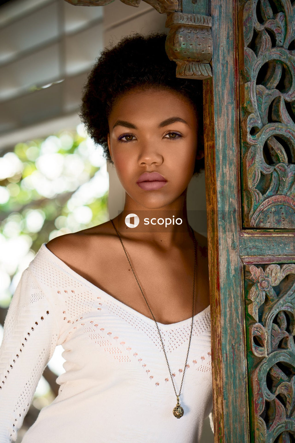 Woman in white top and short hair leaning on carved door