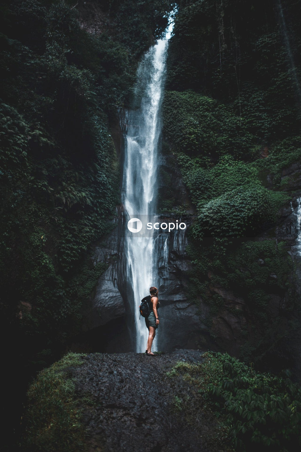 Woman in white tank top standing on rocky waterfalls