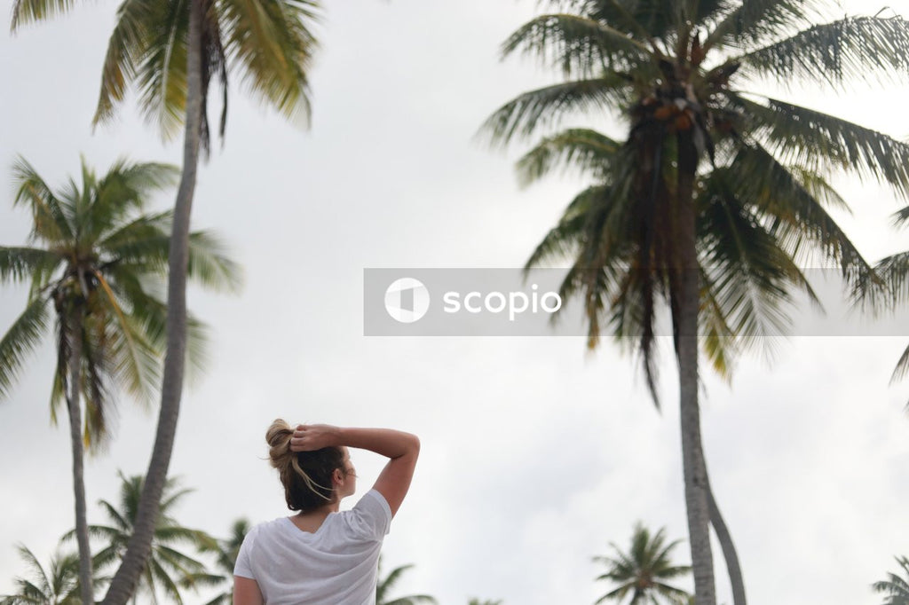 Woman in white t-shirt standing near palm tree