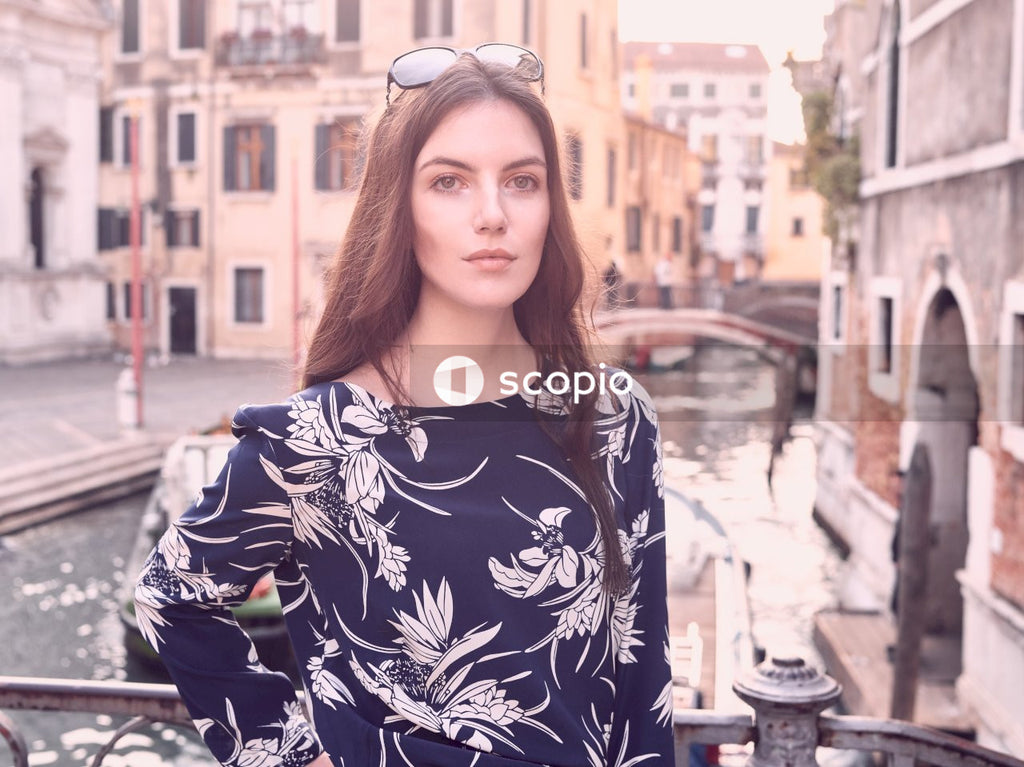 Woman in black and white floral long sleeve shirt standing near brown concrete building