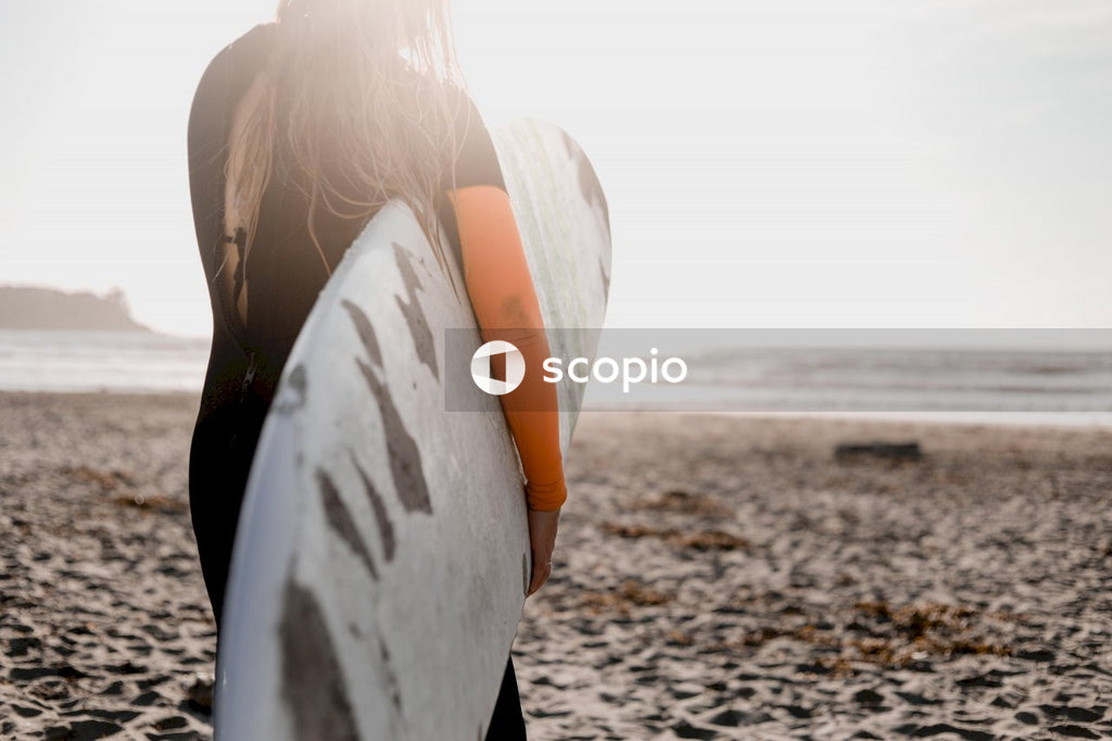 Woman in white shirt and black pants holding white surfboard on beach