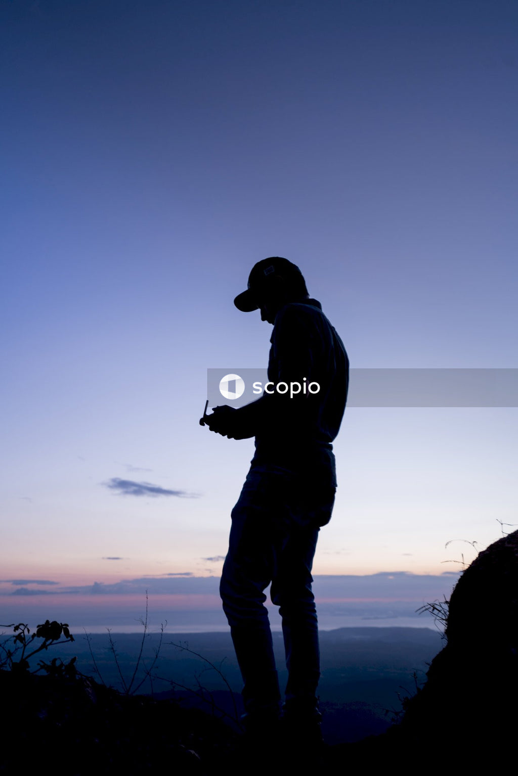 Silhouette of man holding a remote controller on top of mountain during sunset