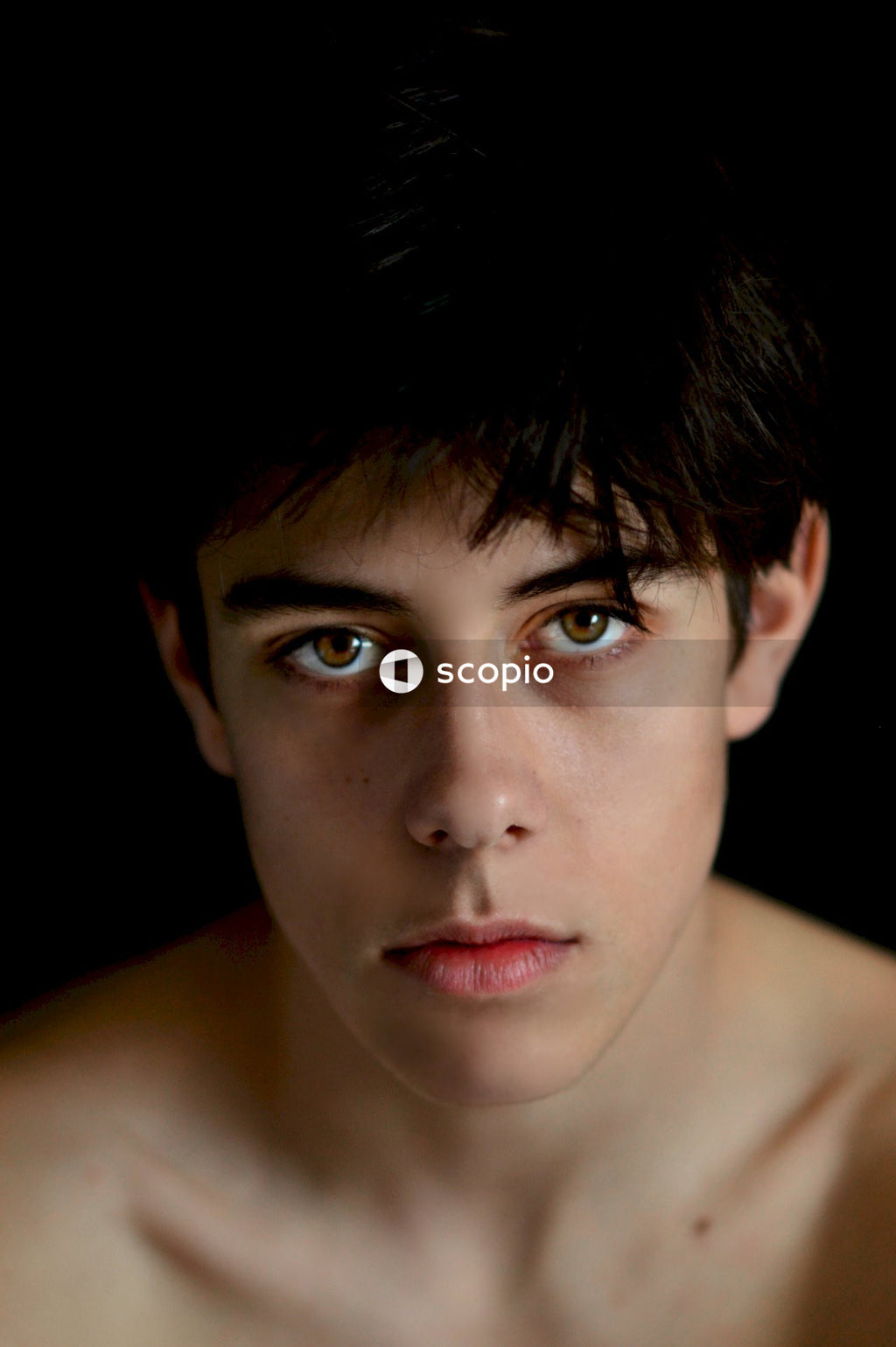 Portrait of topless young man against dark background