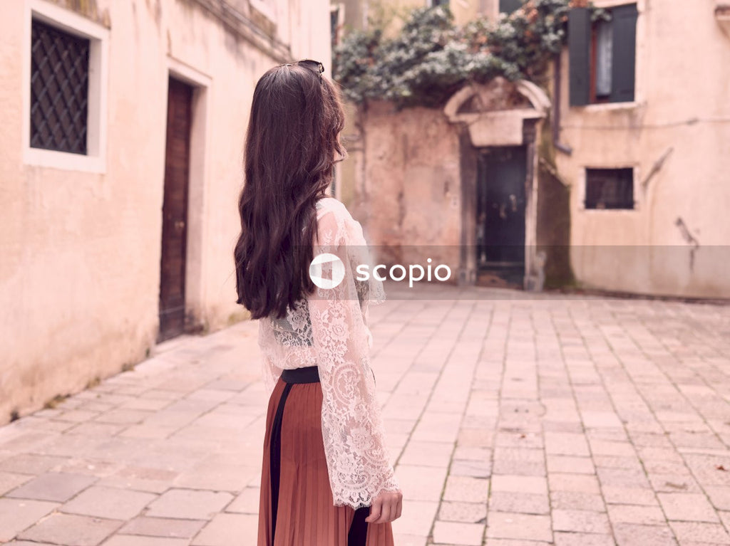 Woman in white lace long sleeve shirt and red skirt walking on sidewalk