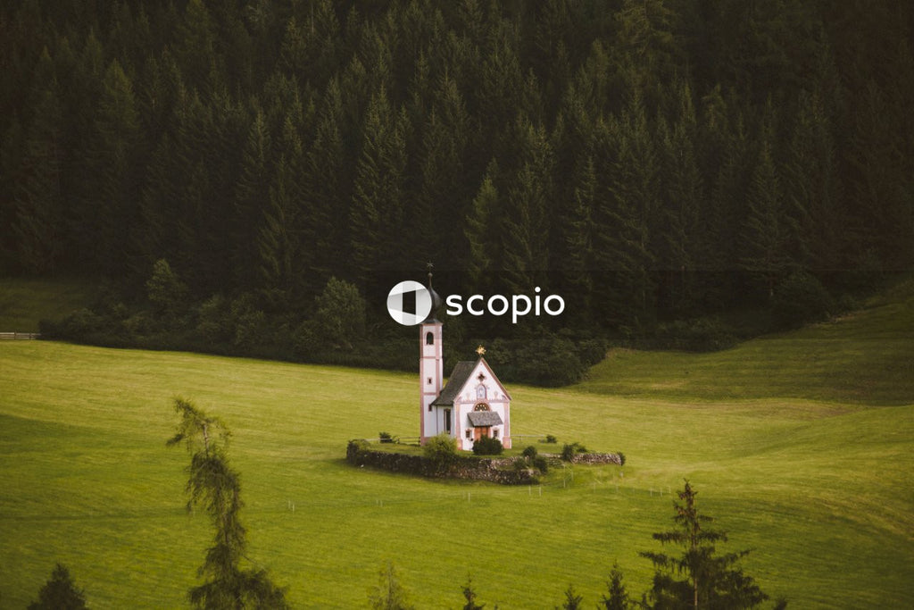 White and black church on green grass field surrounded by green trees