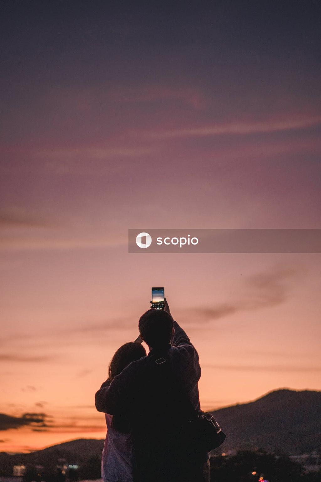 Couple holding smartphone taking a photo of the sunset