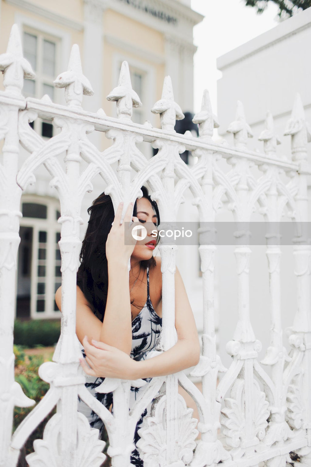 Woman in light and dark jumpsuit behind light building fence
