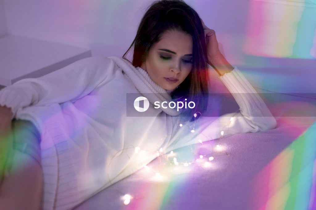 Woman in white shirt lying on white bed in colorfully lit room