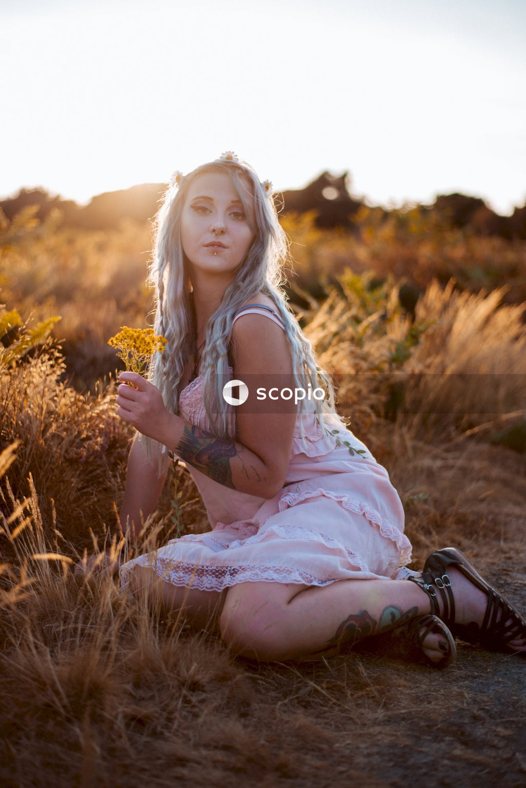 Woman in white sleeveless dress sitting on grass field holding yellow flowers