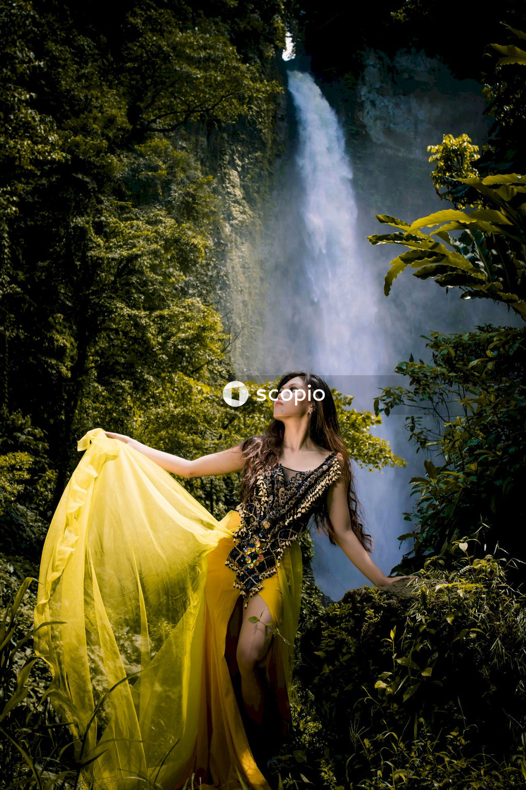 Woman in fancy dress standing beside waterfall