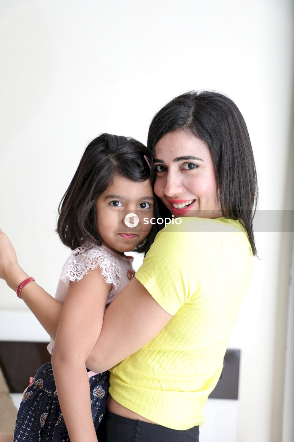 Woman in yellow shirt hugging girl in white floral dress