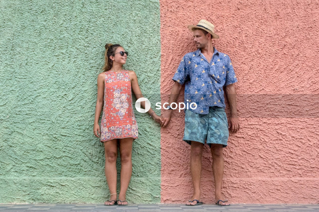 Woman and man in summer outfits holding hands in front of green and red wall