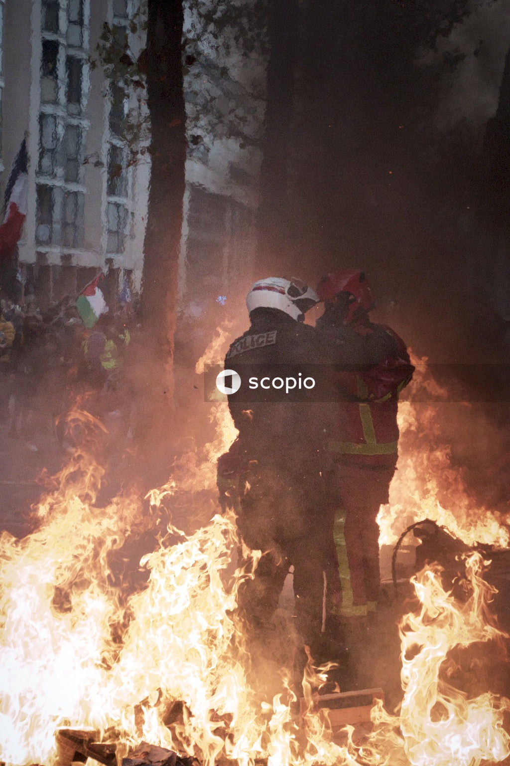 Riot police officer briefing a firefighter amongst flamming barricades