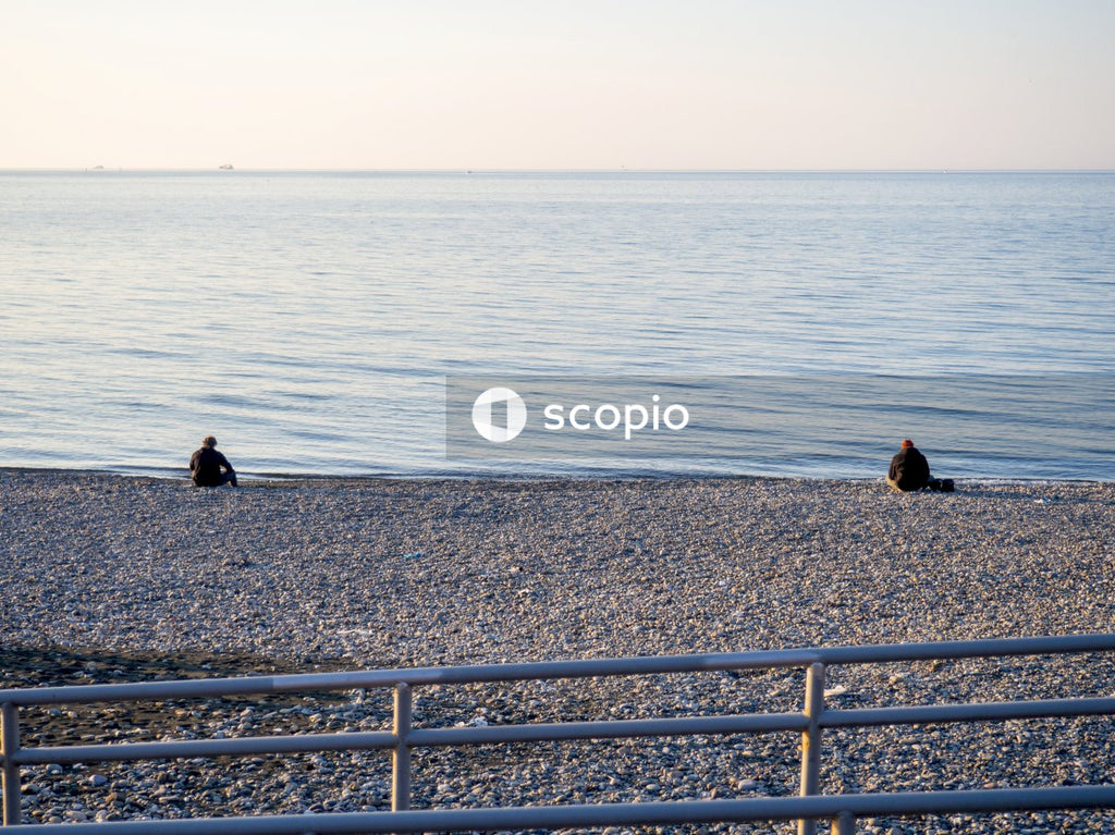 2 people sitting on gray concrete fence near body of water