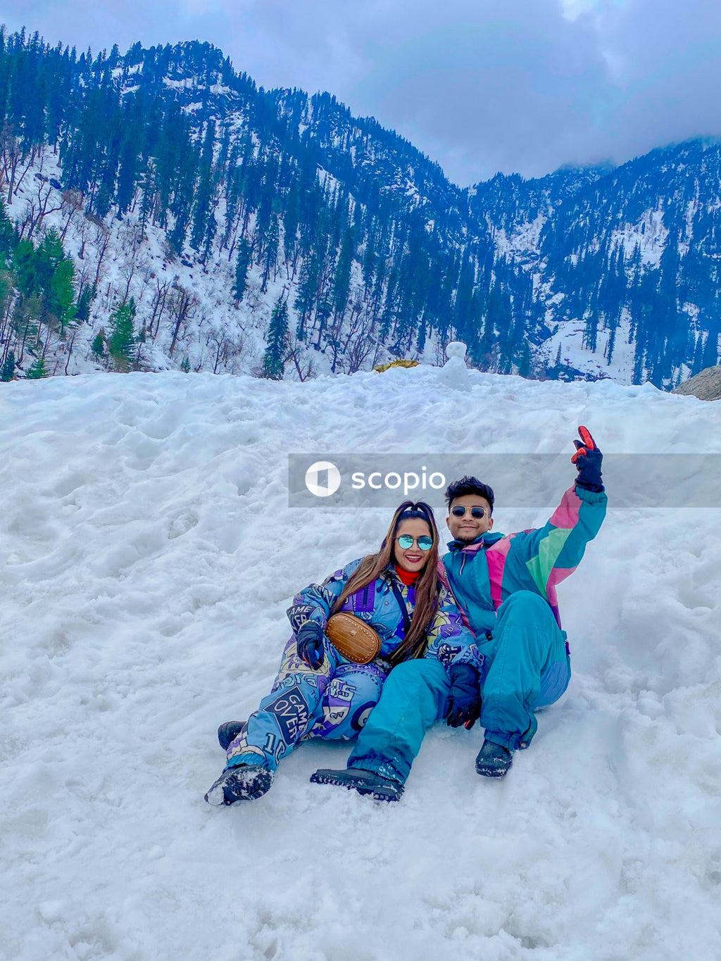 Young South Asian man and woman in skiing outfit sitting on snow covered ground in Solang Valley, Manali, India