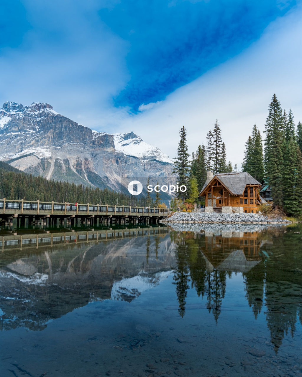 Brown wooden house near lake under snow covered mountain with reflection on water