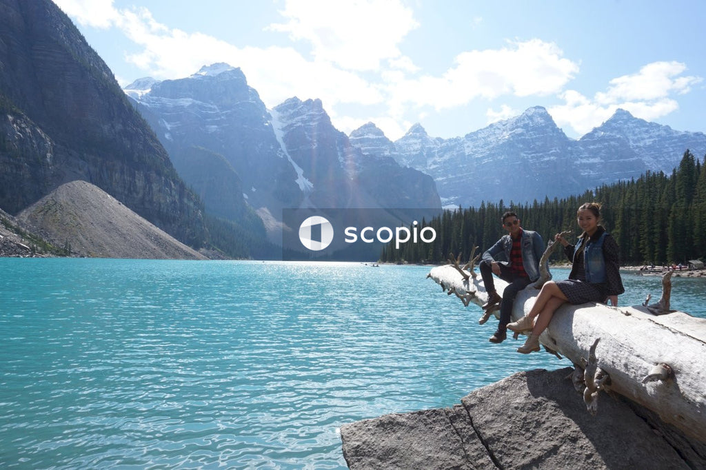 Man and woman sitting on a rock by shoreline of Moraine lake in Alberta, Canada