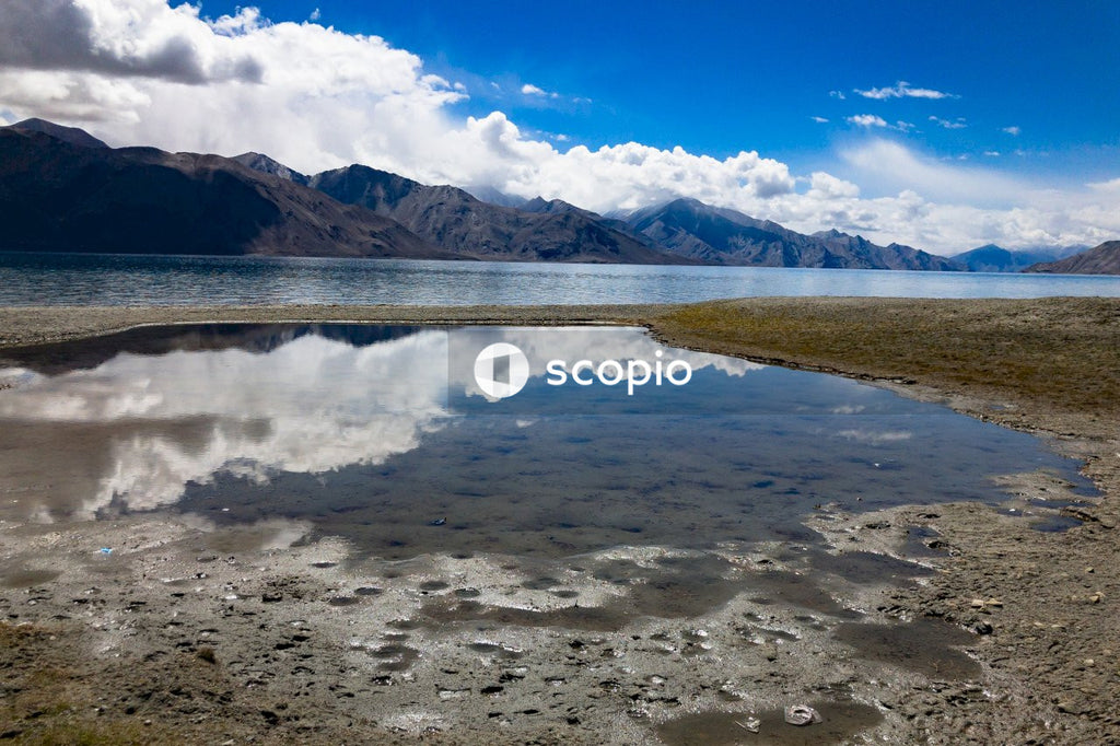 Body of water near mountain under white clouds and blue sky