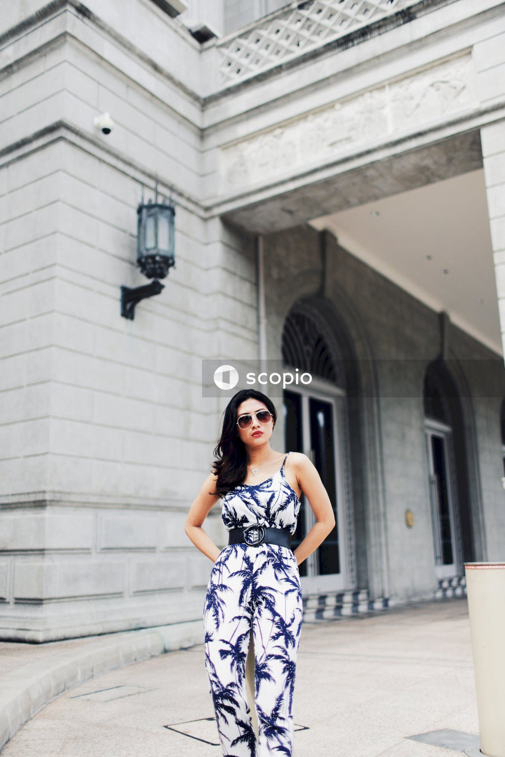 Woman in black and white floral sleeveless dress standing near white concrete building