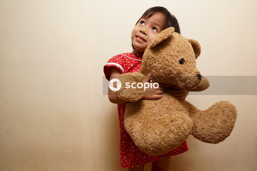 Girl in red and white polka dot shirt hugging brown bear plush toy