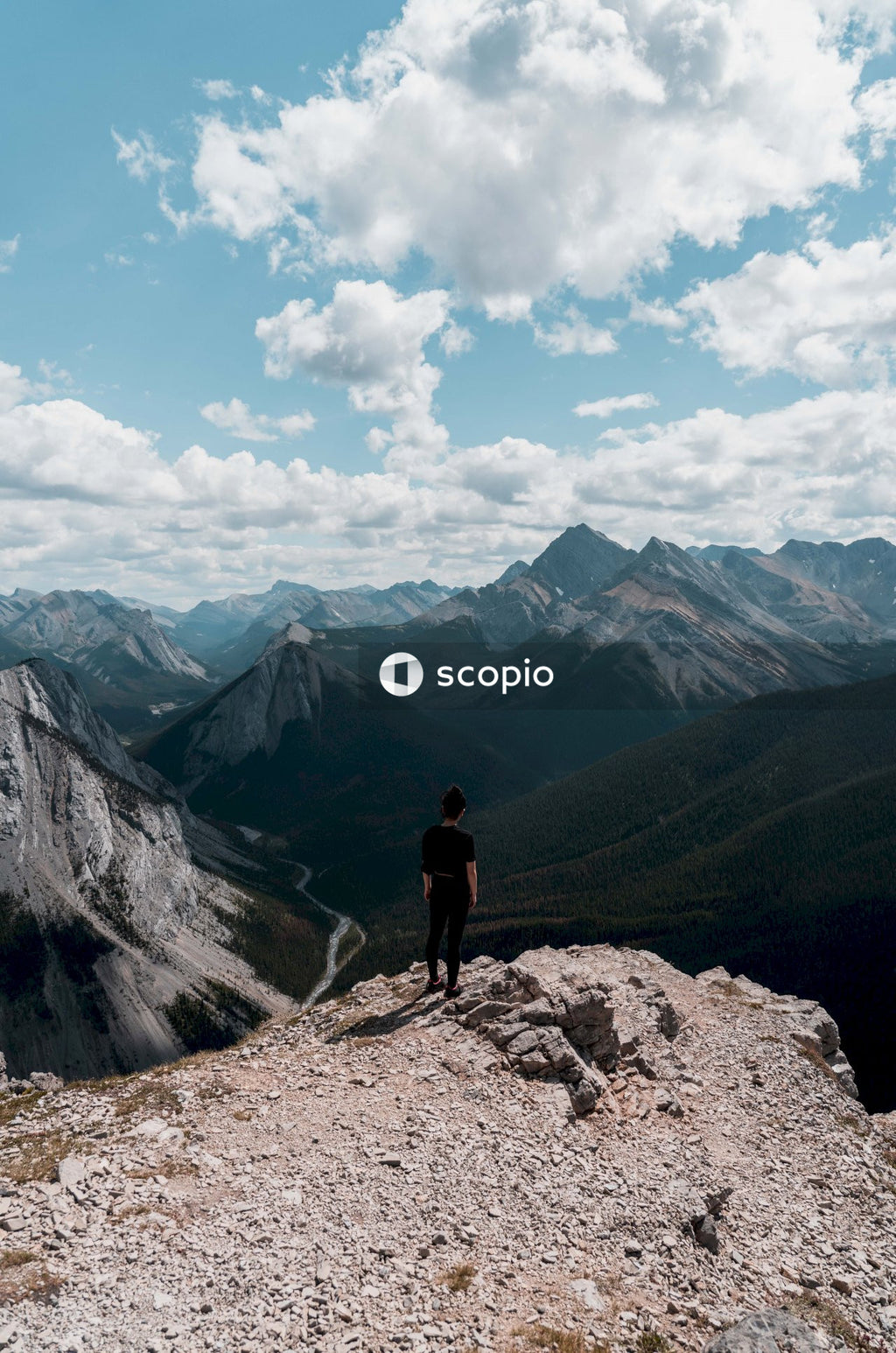 Man in black shirt standing on brown rock mountain under white clouds and blue sky