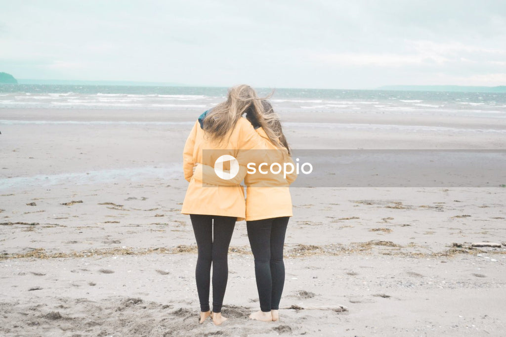Two women in yalloe jacket hugging on shore