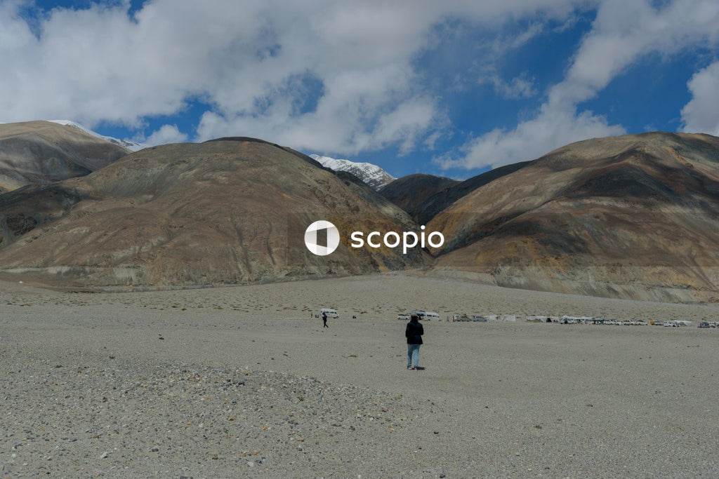 2 people walking on gray sand near brown mountain under white clouds