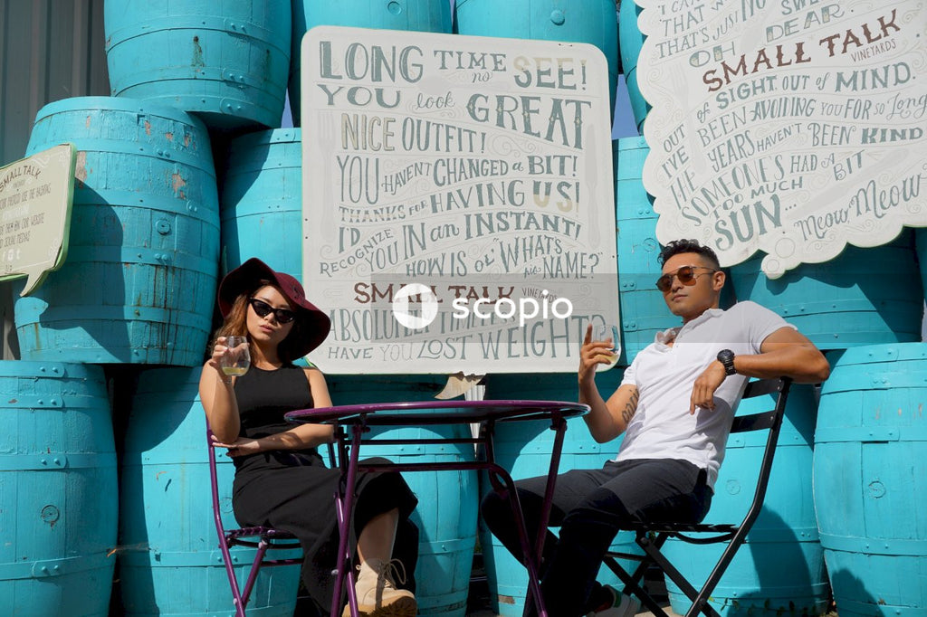 Man and woman sitting at a table beside blue barrels drinking wine