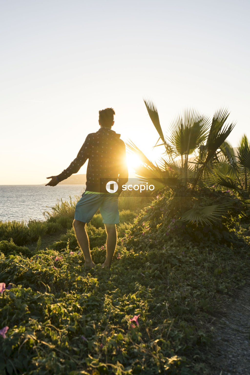 Man in brown shirt and blue shorts standing on green grass field near body of water