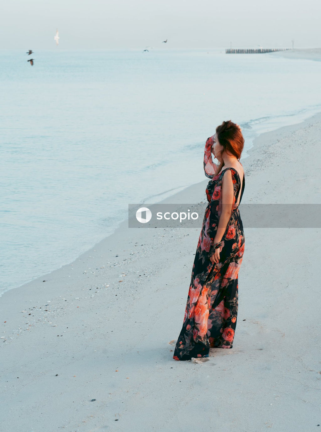 Woman in red and black floral dress standing on beach