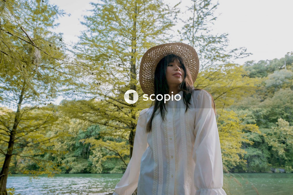 Woman in long sleeve shirt wearing brown straw hat standing near body of water