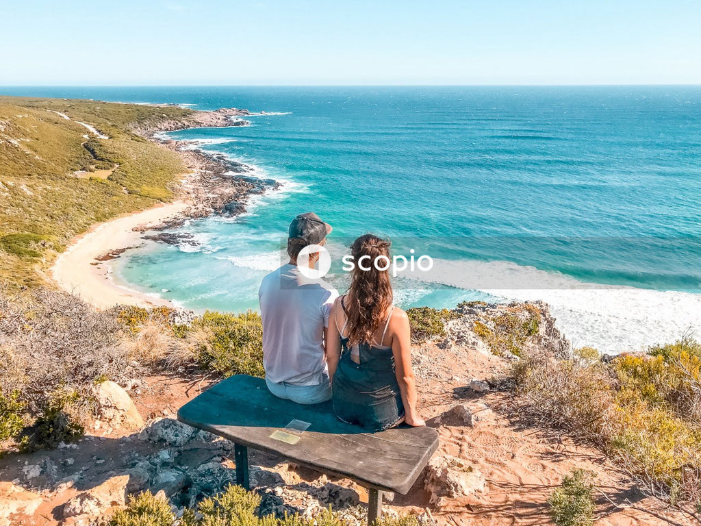 Man and woman sitting on bench on mountain island facing the ocean