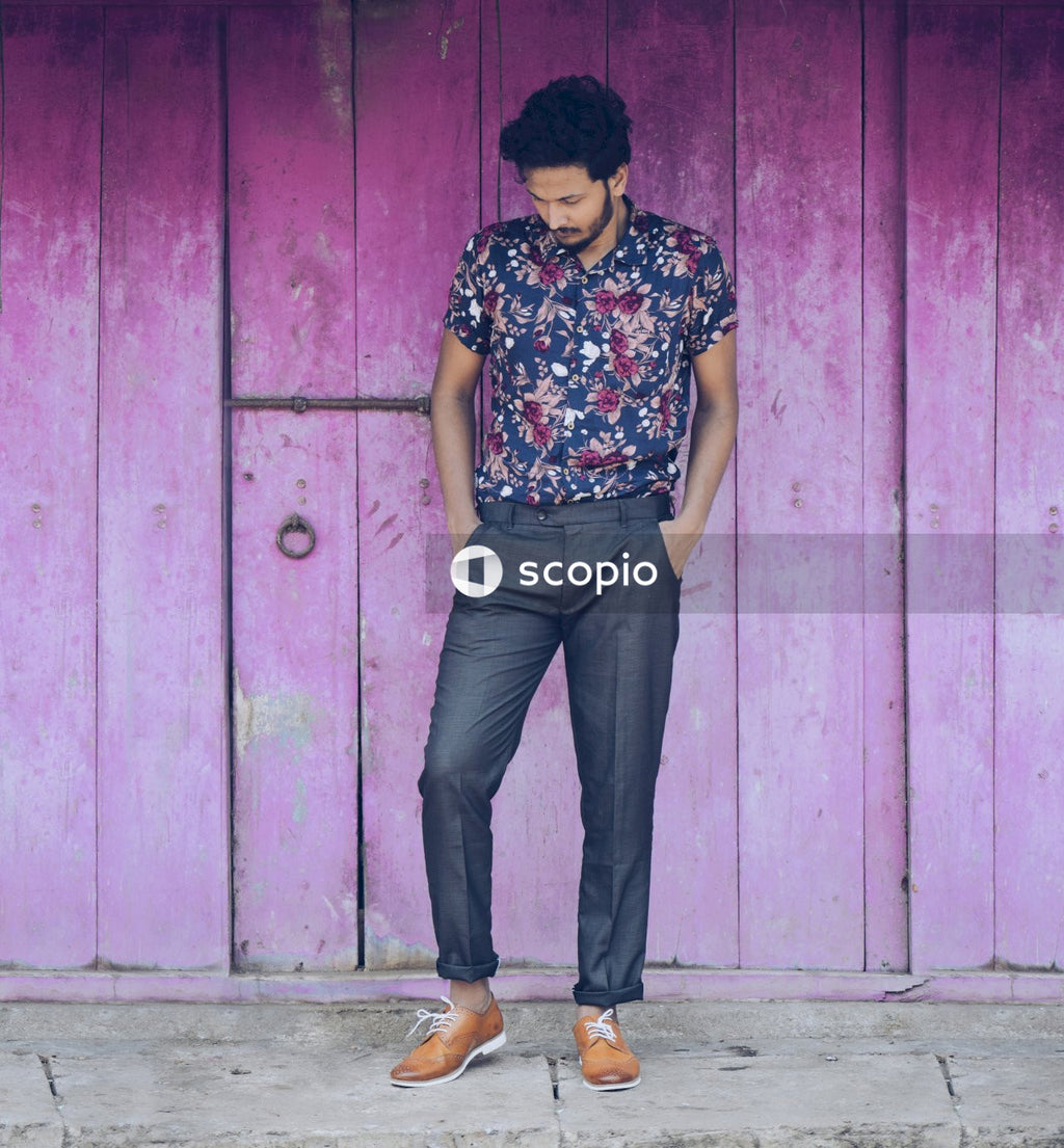 Man in colorful floral t-shirt and dark pants standing beside purple wall