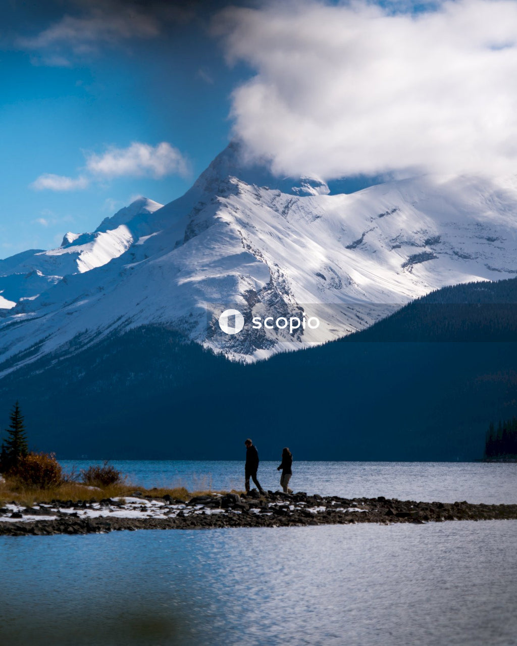 Two people standing on rock near snow covered mountain