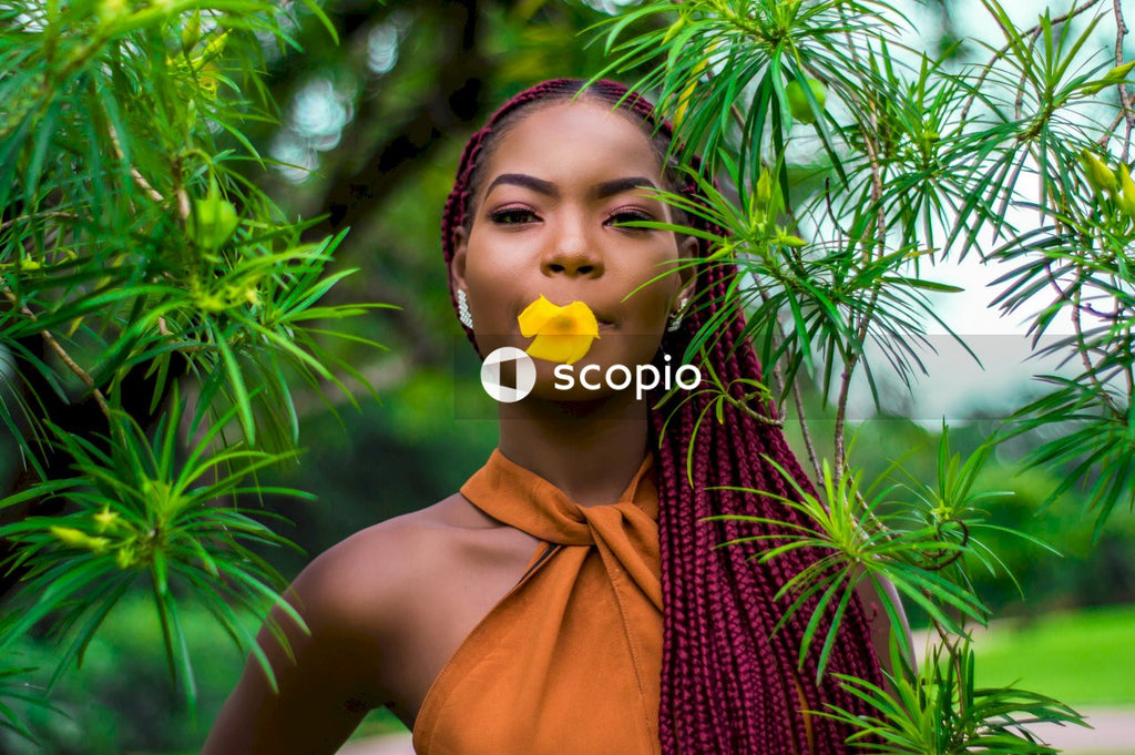 Woman with red braided hair holding yellow flower between her lips